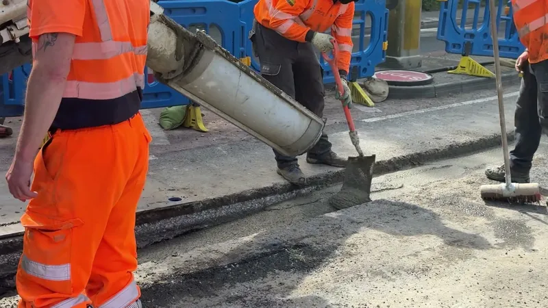 Operative directing the discharge chute into an open utility trench while the gang strikes off the fill